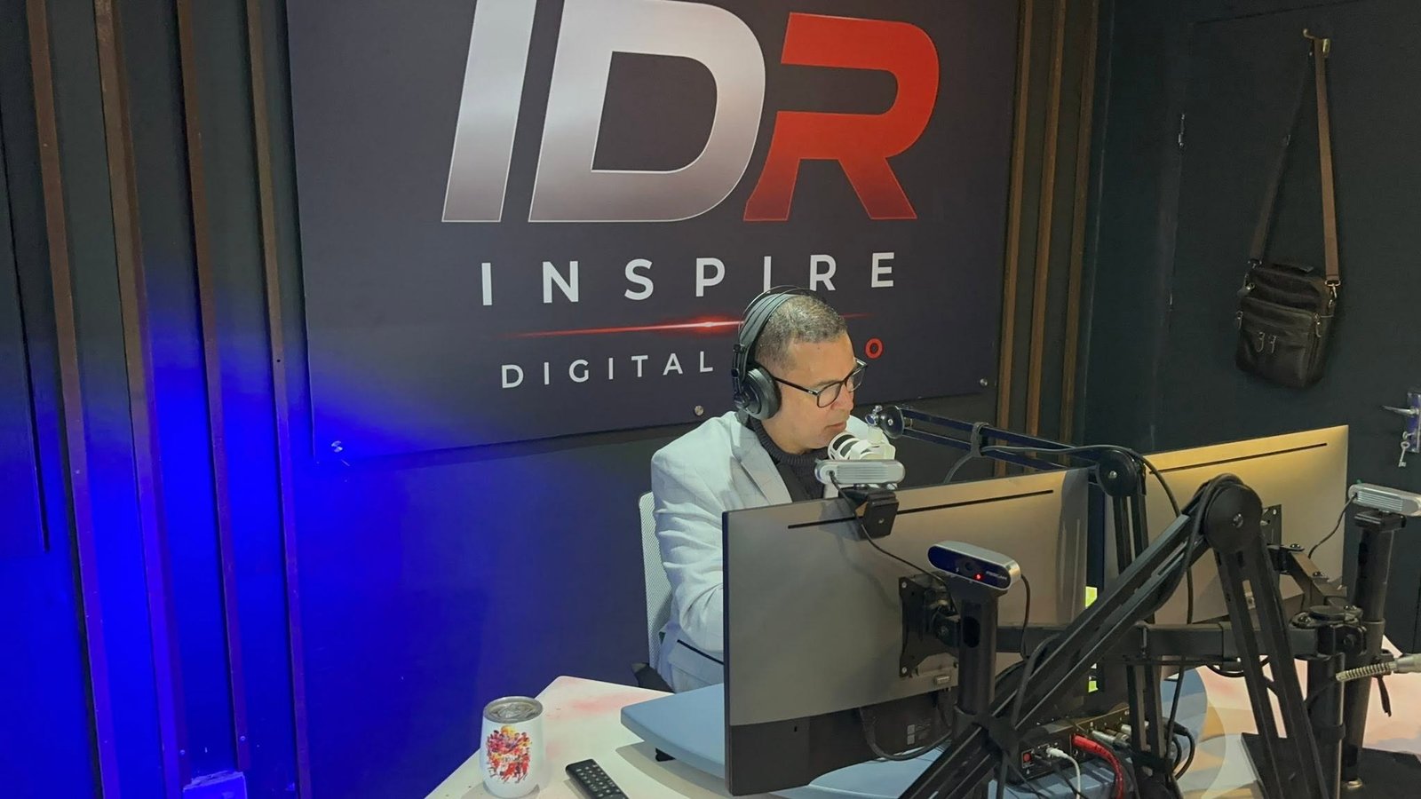 An Inspire Digital Radio presenter on air in front of the studio's branded wall